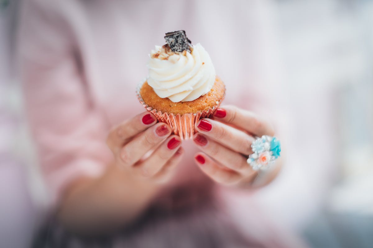 8 Worst Foods Diabetics Should Avoid at All Costs 3 A close-up of a woman's hands holding a creamy frosted cupcake, showcasing indulgence and sweet delight.
