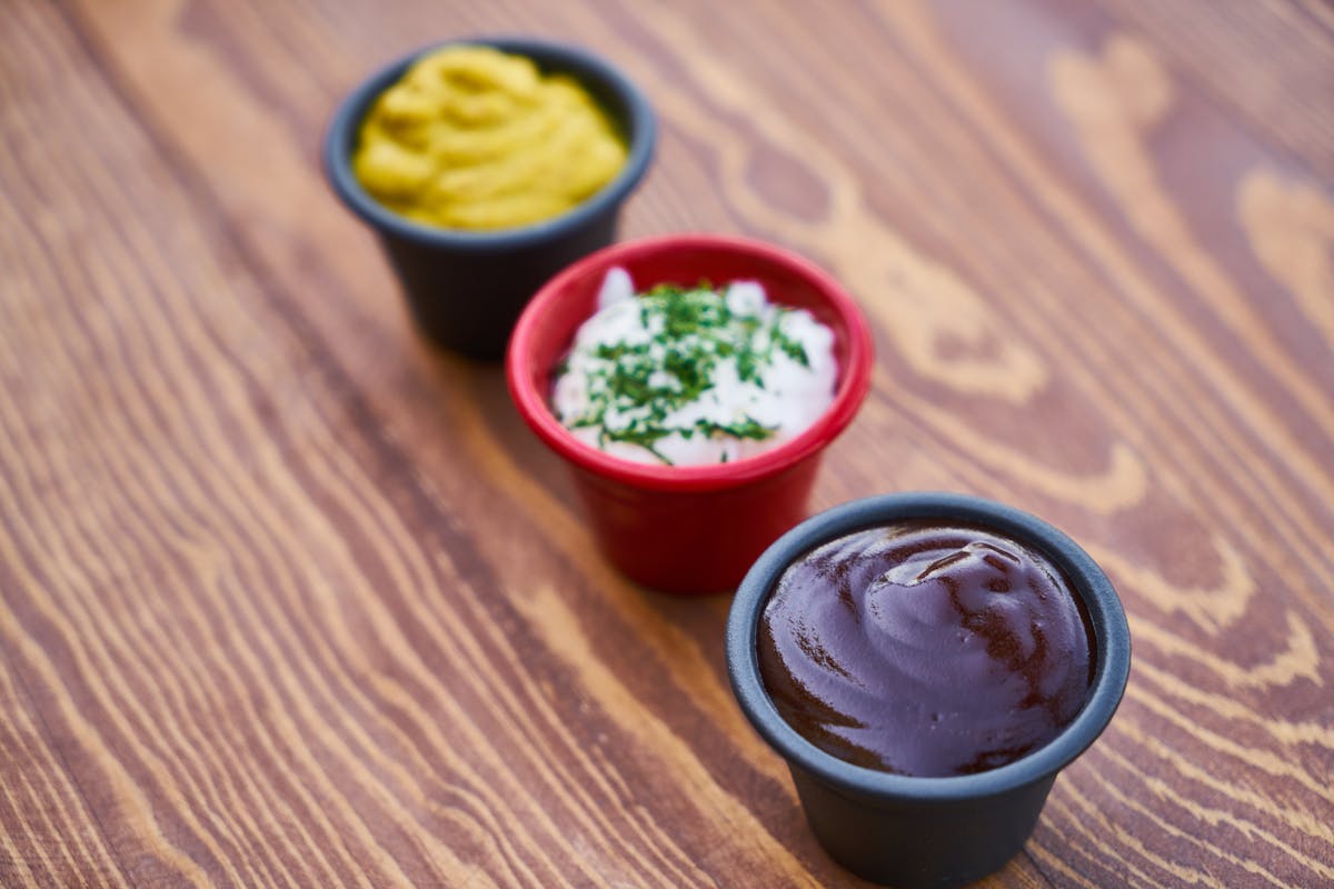 The Wildest Food and Condiment Mishaps That Escalated Into Chaos 4 A close-up of three sauces in cups on a wooden surface, arranged in line.
