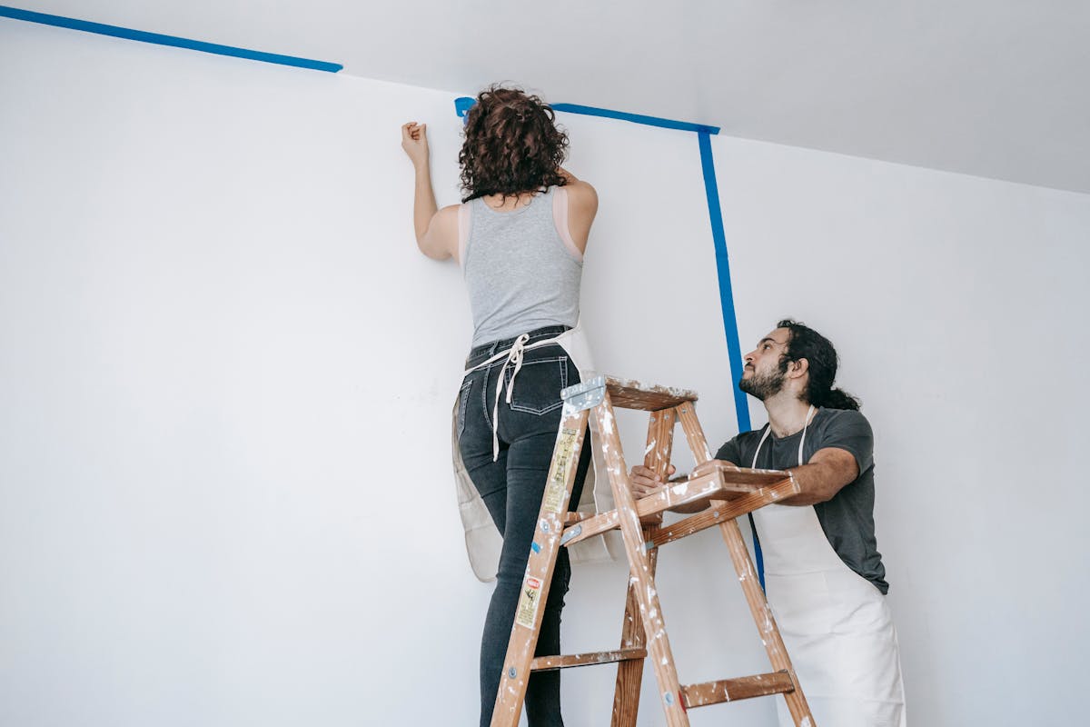 10 Expensive Mistakes to Avoid When Buying a Home 4 A couple collaborates on home renovation with paint and ladder.