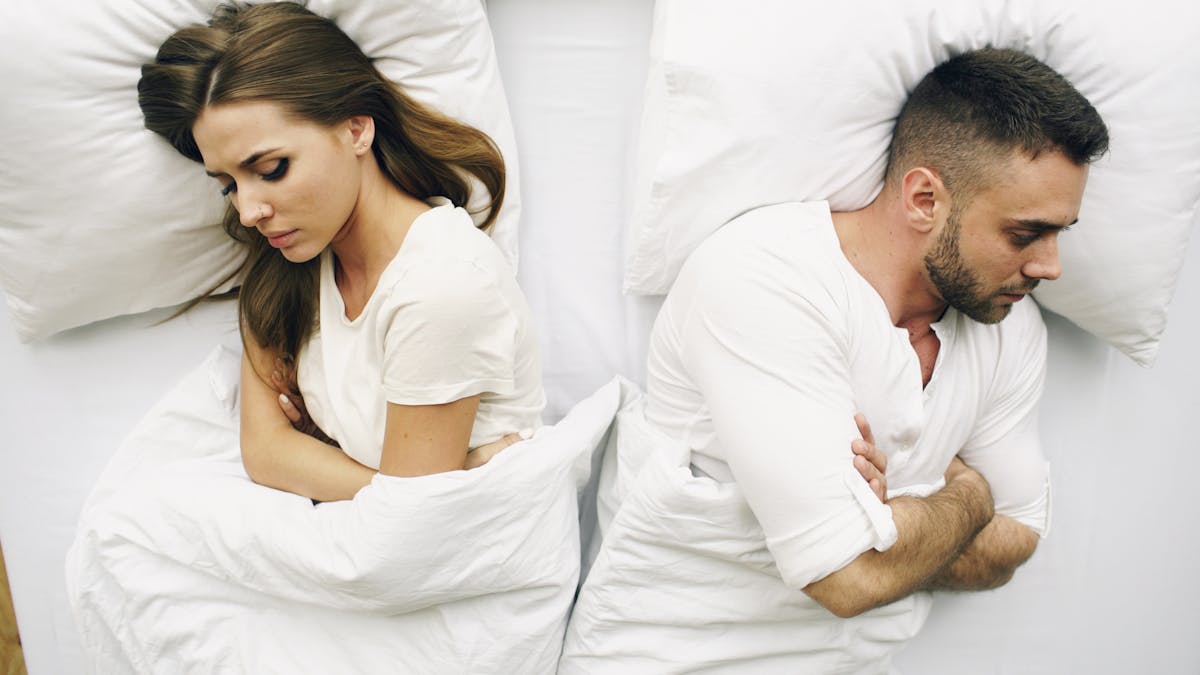 9 Mistakes Couples Make That Lead to Breakups 1 A couple lying in bed facing away, expressions of discontent.