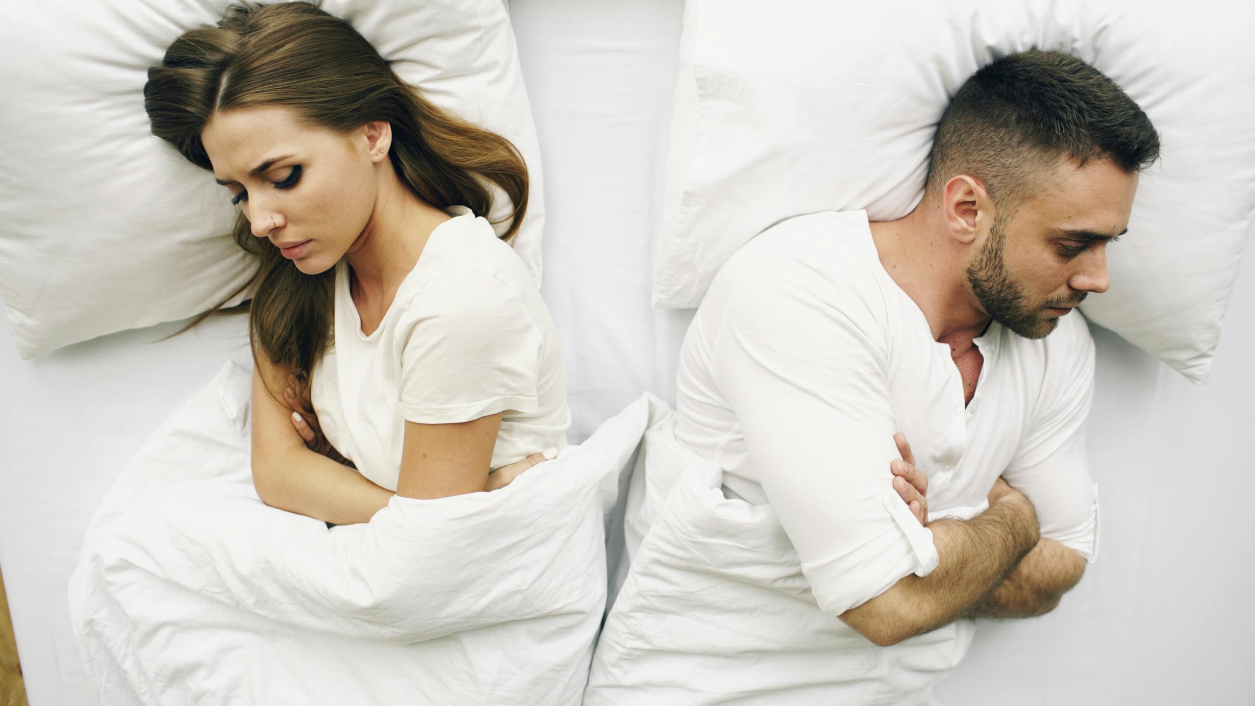 8 Warning Signs Your Relationship Is Quietly Falling Apart 3 A couple lying in bed facing away, expressions of discontent.