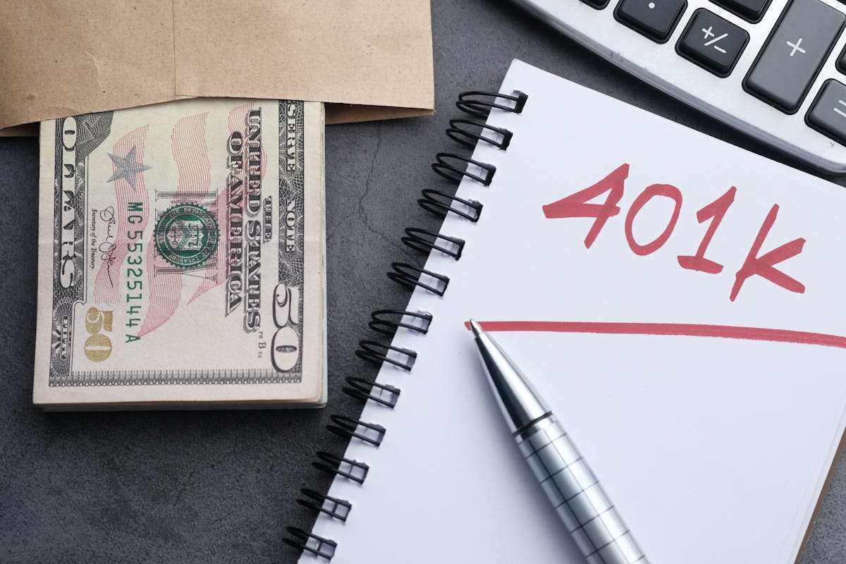 8 Money Mistakes You Need to Avoid to Protect Your Financial Future 2 A desk setup with a notebook labeled '401k', a pen, cash, and a calculator representing financial planning.