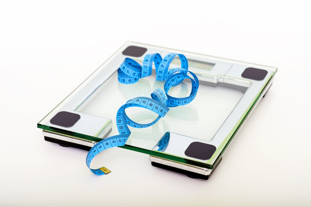 10 Mistakes To Avoid If You Want To Lose Weight 2 A digital glass weighing scale with a blue measuring tape, symbolizing weight management.