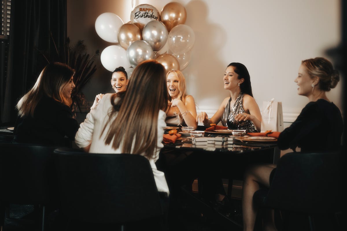 10 Signs You're Definitely The Mooch Of Your Friend Group 2 A group of joyful women celebrating a birthday with balloons indoors.