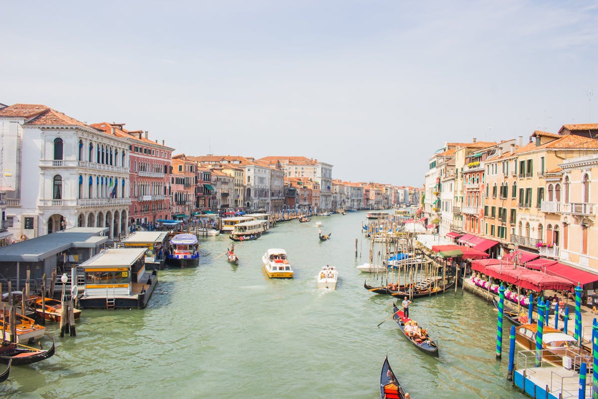 7 Overcrowded Destinations to Skip This Summer 1 A lively view of Venice's Grand Canal featuring gondolas and historic architecture.