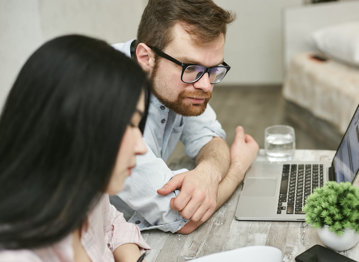 7 Travel Mistakes That Could Ruin Your Entire Trip 4 A man and woman sitting at a table reviewing documents on a laptop indoors.