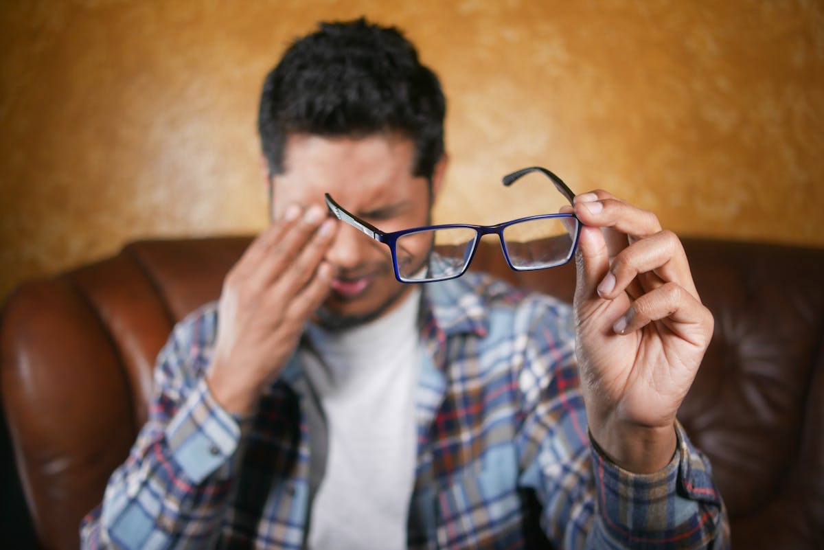 8 Odd Health Symptoms We Should Never Ignore 3 A man in plaid shirt holding eyeglasses indoors. Focus on eyewear with neutral background.