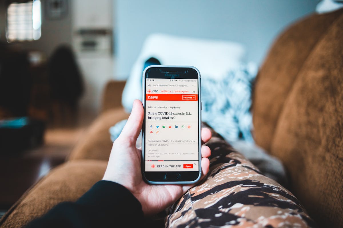 10 Unhealthy Habits That Are Undermining Your Well-being 3 A person browsing news on a smartphone while relaxing on a sofa indoors.