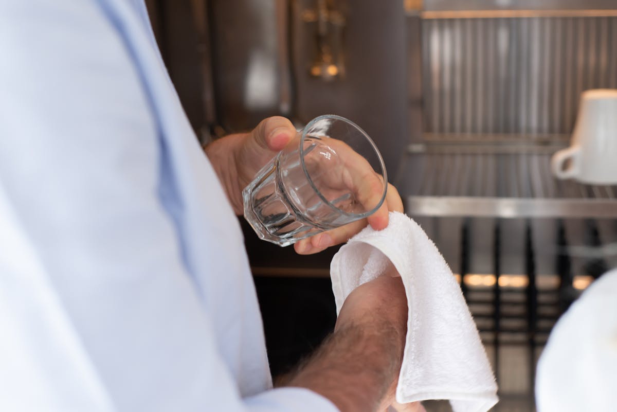 8 Spring Cleaning Mistakes You’re Probably Making 1 A person drying a glass with a towel in an indoor kitchen setting.