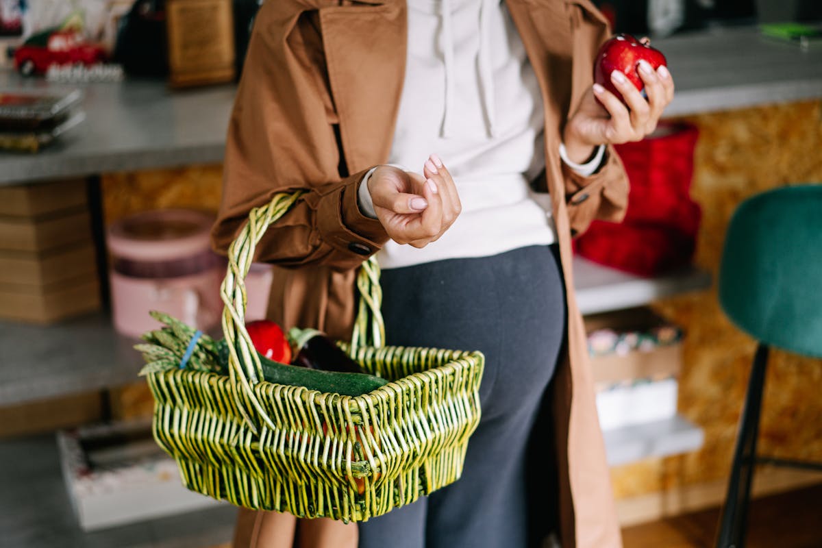 10 School Facts Boomers Learned That Turned Out to Be Wrong 4 A pregnant woman holds a green wicker basket filled with fresh apples indoors.