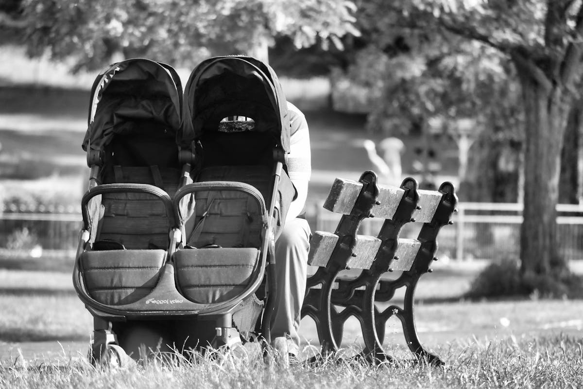 10 Parenting Habits That Drain Your Budget 1 A serene black and white image of a stroller next to a park bench in a peaceful outdoor setting.