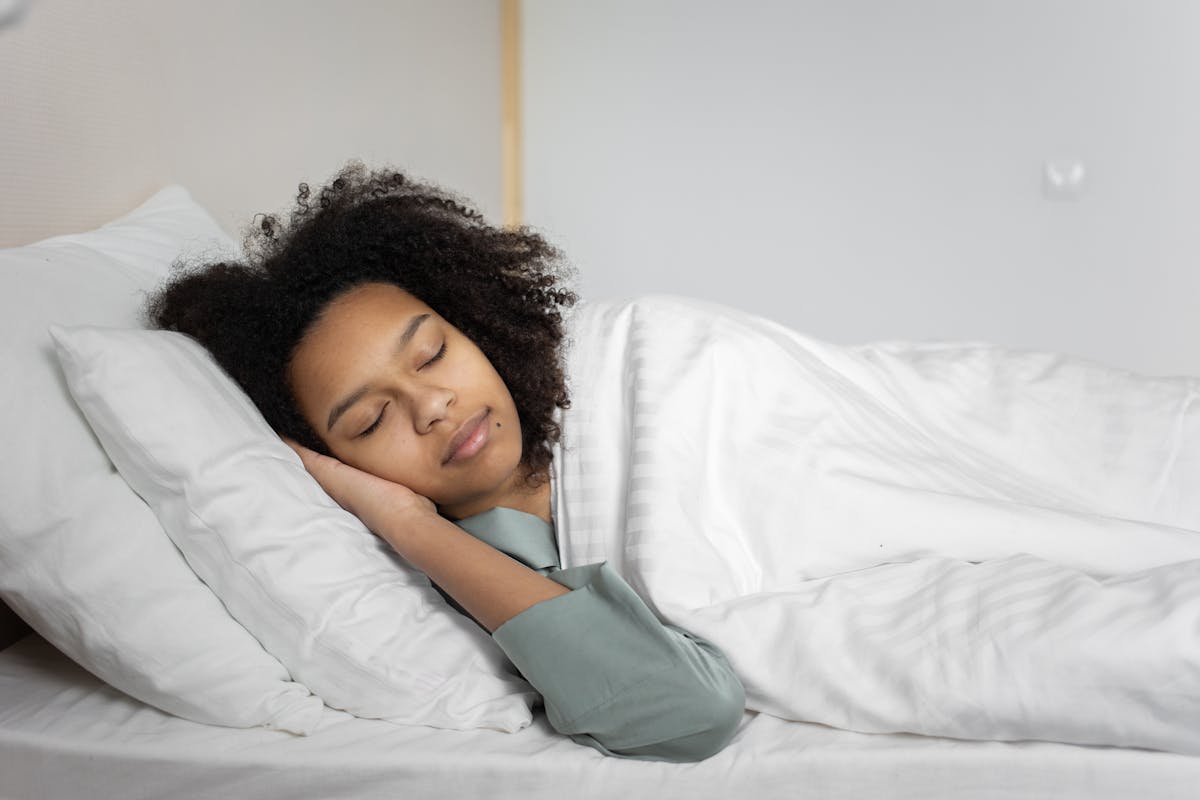 9 Cheap Ways to Boost Your Happiness 4 A serene scene of a woman with afro hair peacefully sleeping in a cozy bedroom.