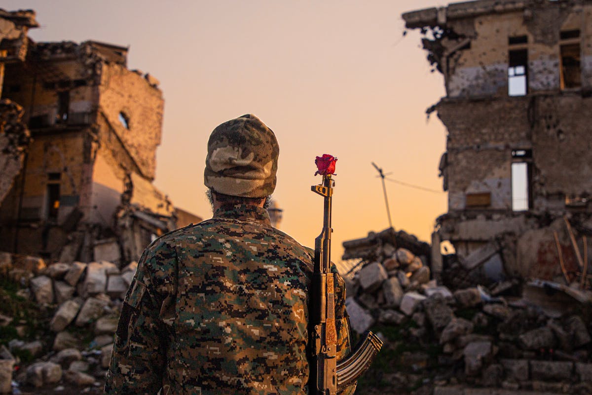 10 Most Dangerous Cities in the World to Avoid in 2026 1 A soldier in camouflage with a red rose on rifle amidst ruined buildings at sunset.