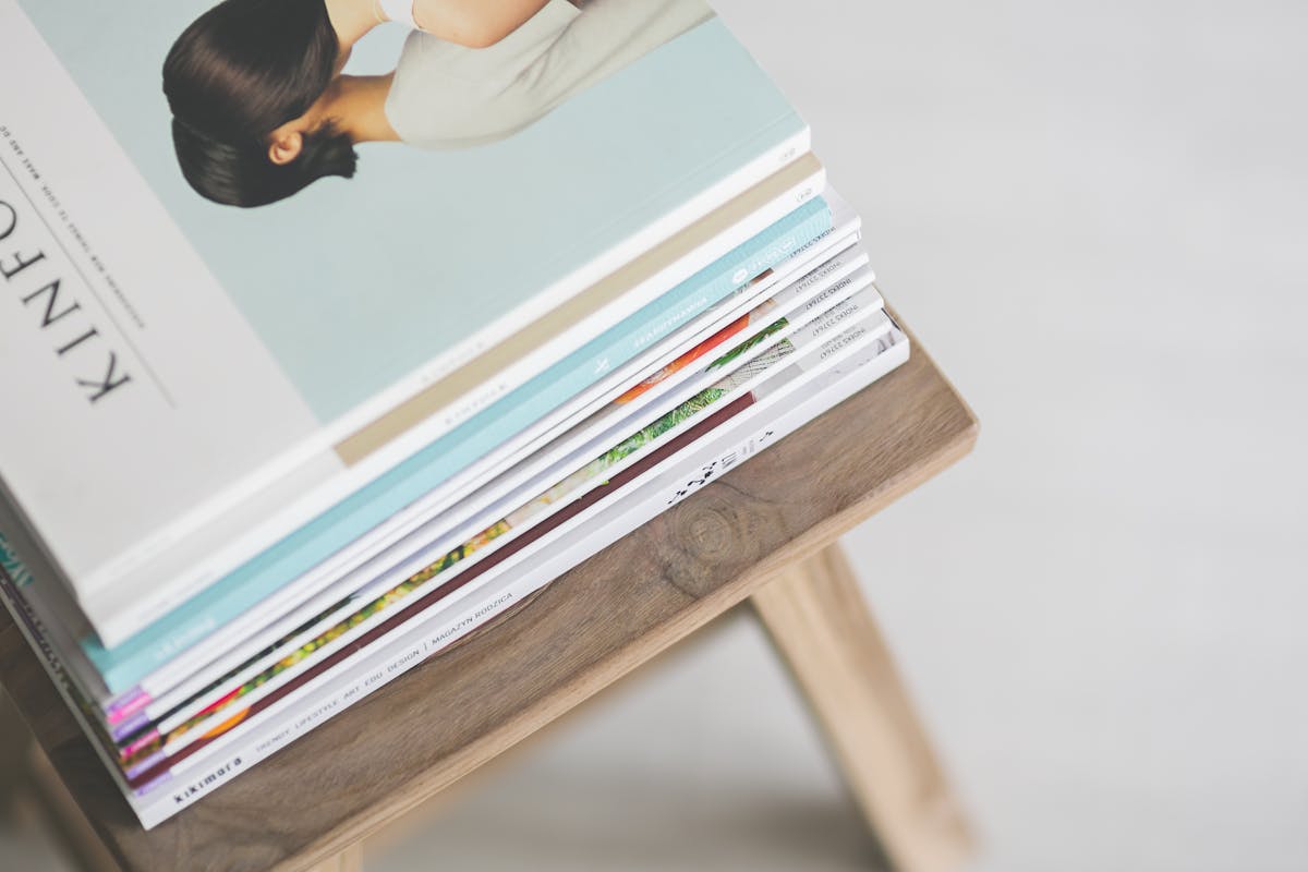 10 Ways to Stop Wasting Money Right Now 1 A stack of modern magazines on a wooden stool, perfect for cozy reading.