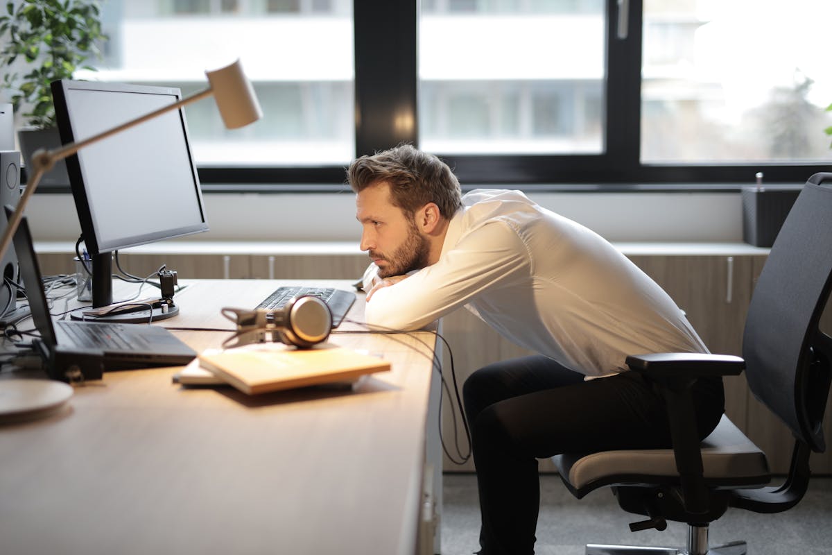 10 Ways People Got Paid to Do Nothing 2 A tired man leaning on his desk in a modern office, looking at the computer screen.