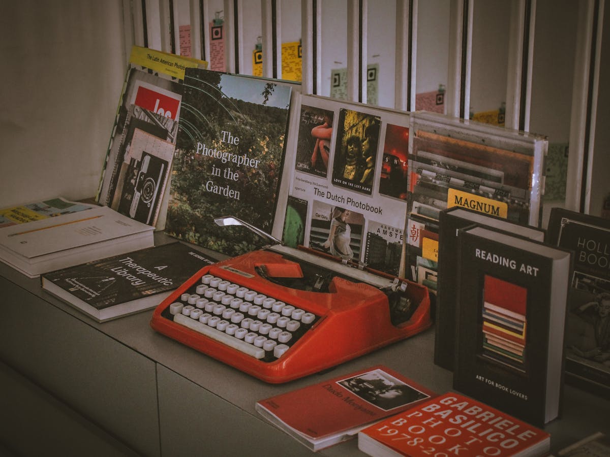 9 Strangest Celebrity Collections 3 A vibrant red vintage typewriter surrounded by a collection of photobooks and literature in an artistic setup.