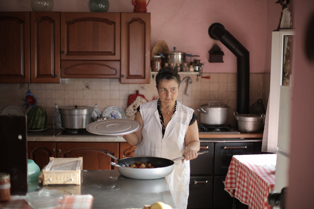 10 Ways to Stop Wasting Money Right Now 3 A woman cooking at home, showcasing culinary skills in a rustic kitchen setting.