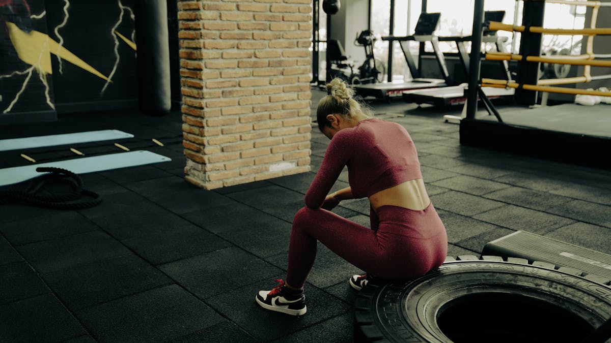 10 Mistakes To Avoid If You Want To Lose Weight 1 A woman in sportswear rests on a tire during gym training, showcasing fitness dedication.