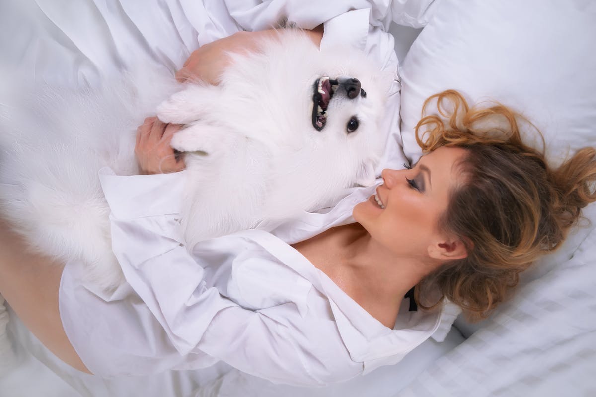 10 Common Allergies That You Shouldn’t Ignore 2 A woman lovingly embraces a Pomeranian dog on a cozy white bed.