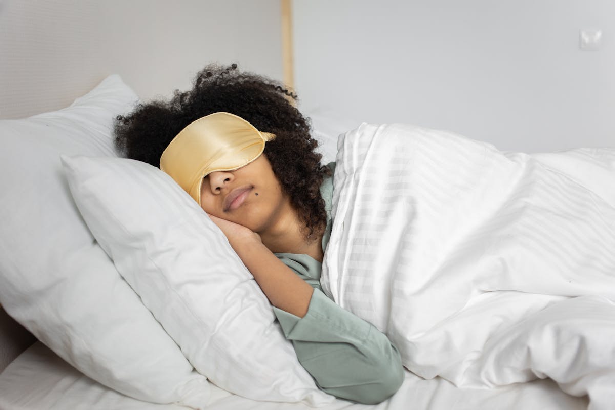 8 Time-Draining Things That Will Exhaust You As A Parent 3 A woman with afro hair sleeps soundly in bed with a sleep mask, enjoying a cozy indoor atmosphere.