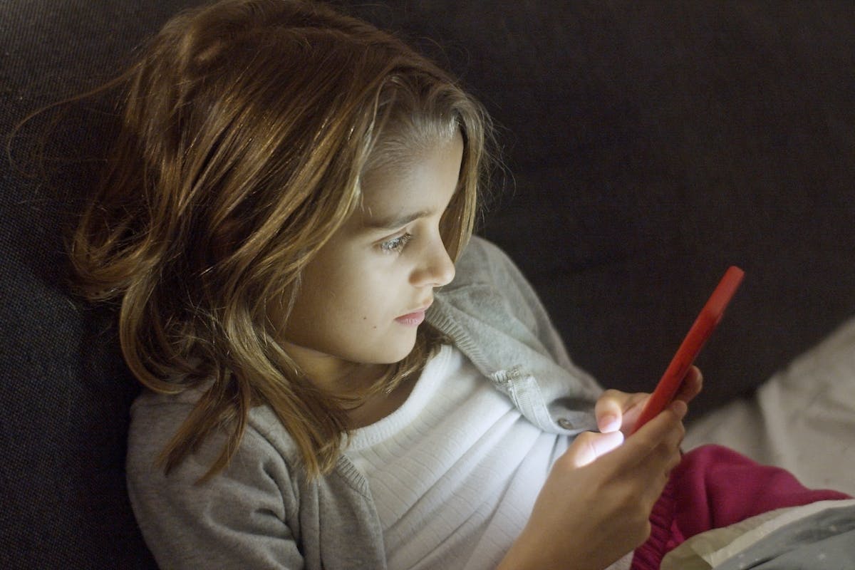 8 Time-Draining Things That Will Exhaust You As A Parent 2 A young girl with blond hair uses a smartphone in bed at night.