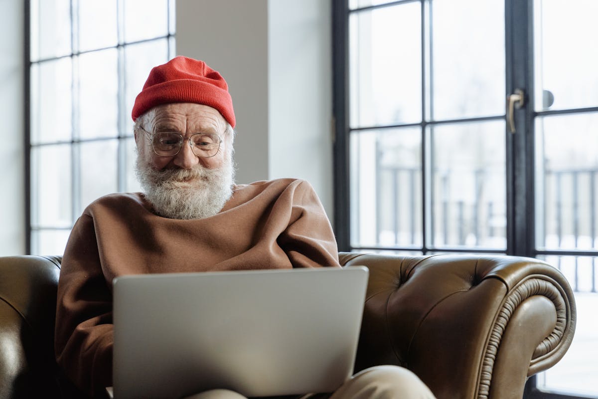 10 Common Scams Targeting Seniors and How to Avoid Them 3 An elderly man with a beard uses a laptop in a cozy indoor setting, smiling contently.