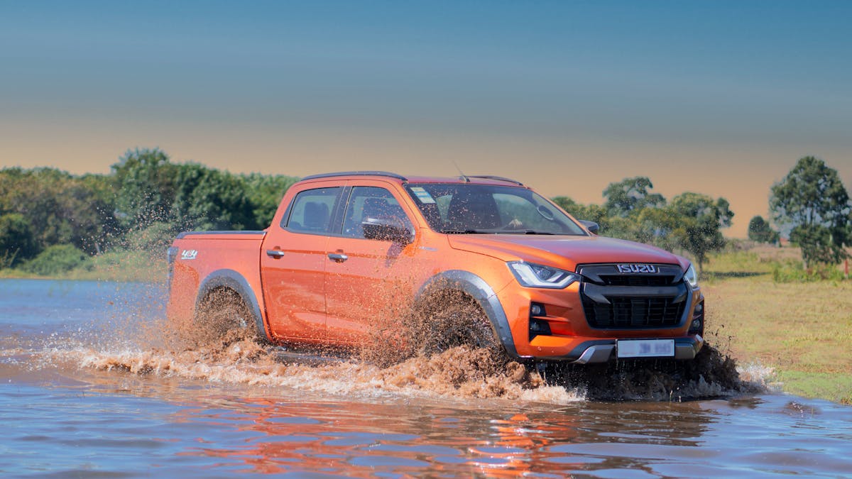 10 People Who Should Not Buy a Truck 2 An orange Isuzu D-Max pickup truck splashing through water in a rugged terrain.