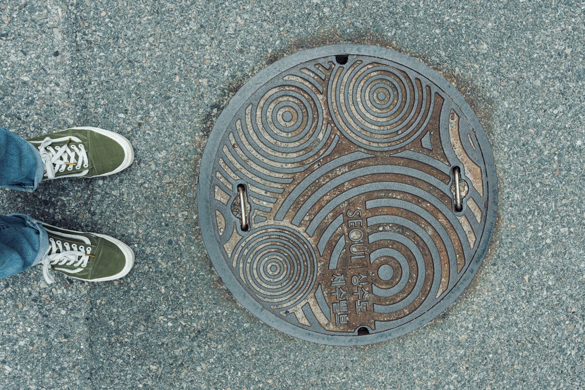 10 Bizarre Explosions That Will Leave You Speechless 2 Artistic sewer cover design on a Seoul street with green sneakers visible.
