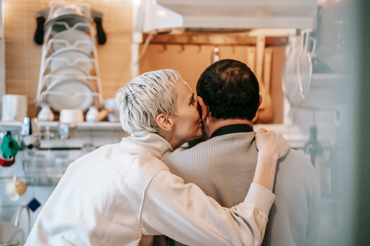 11 Hidden Factors That Could Be Ruining Your Choice of Partner 1 Back view of happy adult woman with short blond hair in casual clothes kissing cheek of anonymous husband while standing together in kitchen
