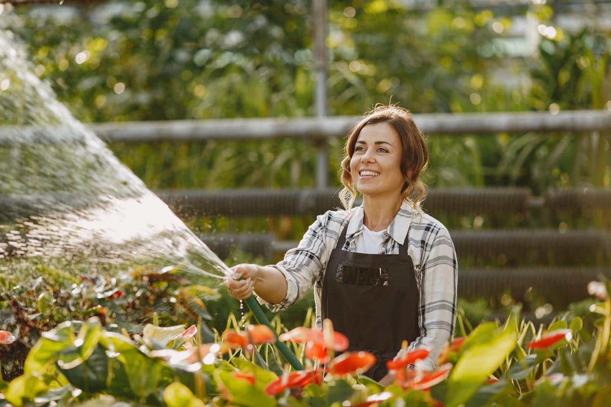 9 Cheap Ways to Boost Your Happiness 1 Cheerful female gardener watering plants in a lush, green greenhouse.