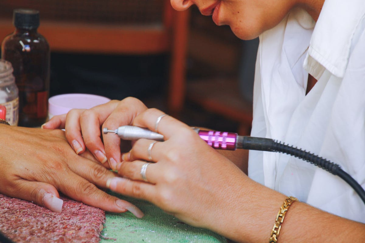9 Mistakes to Avoid When Preparing for Summer 3 Close-up image of a nail technician using an electric file on a client's nails during a manicure session.