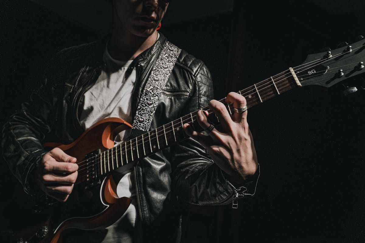 10 Heavy Metal Scandals That Shaped the Genre 2 Close-up of a guitarist strumming an electric guitar in a dark setting, wearing a leather jacket.
