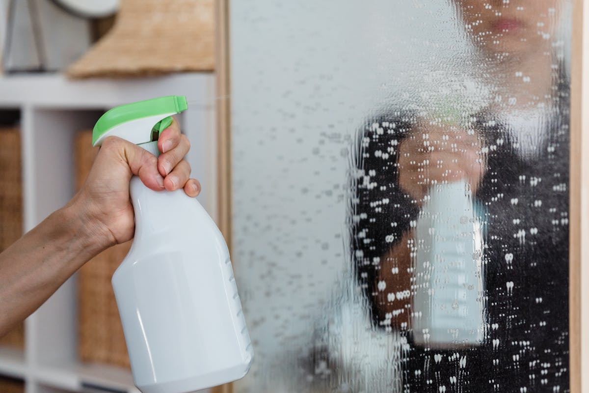 Stop Using These 11 Everyday Items the Wrong Way 3 Close-up of a hand using a spray bottle to clean a mirror indoors.