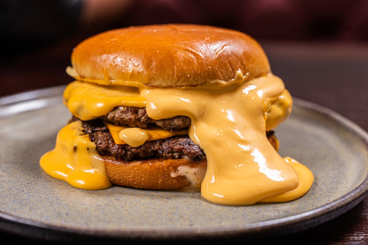 9 Surprising Facts About American Cheese That Will Blow Your Mind 1 Close-up of a juicy burger with thick melted cheddar cheese, served on a plate.