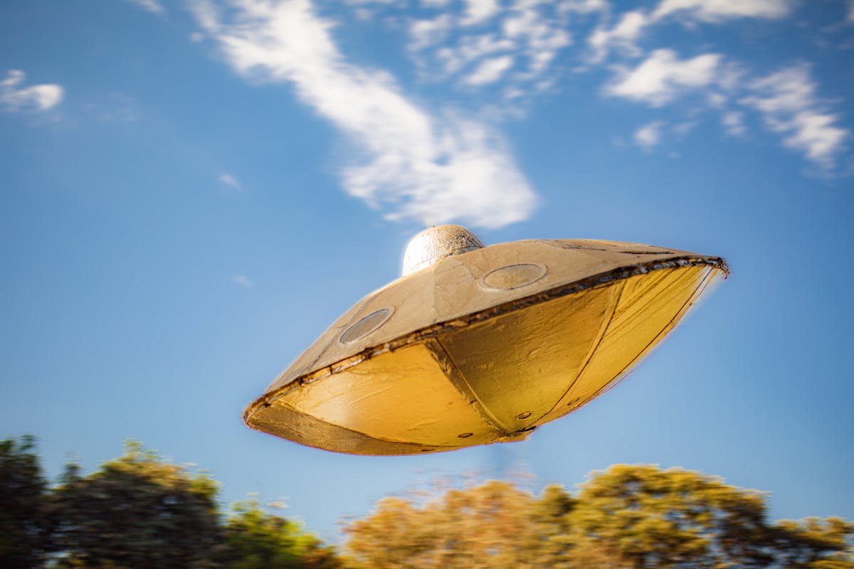 10 Towns in the U.S. That Feel Too Weird to Be Real 2 Close-up of a metallic UFO model flying against a clear blue sky background.