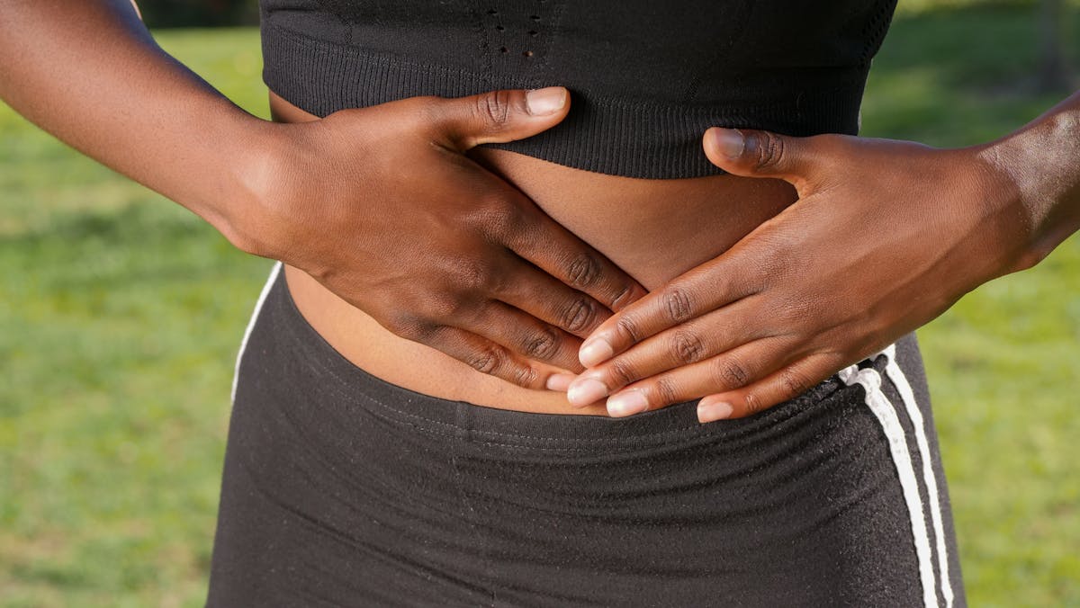 10 Unusual Signs Your Body Is Healthier Than You Think 1 Close-up of a person holding their stomach, indicating abdominal pain outdoors.