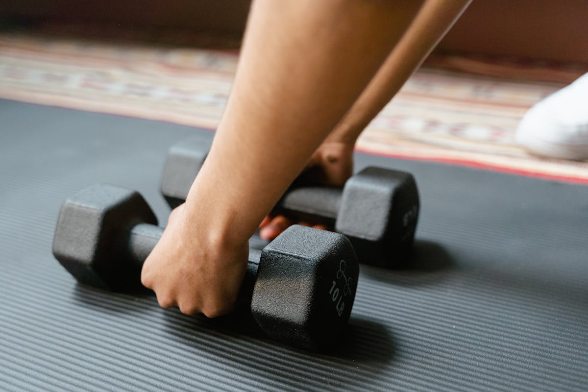Stop Letting These 12 Sneaky Subscription Charges Drain Your Bank Account 3 Close-up of a person picking up dumbbells on a yoga mat, emphasizing fitness and exercise.