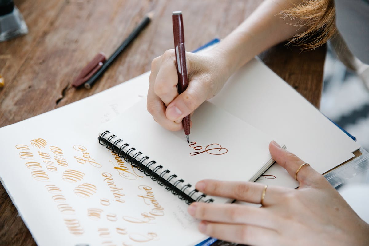10 School Facts Boomers Learned That Turned Out to Be Wrong 3 Close-up of a person practicing calligraphy on a spiral notepad on a wooden table.