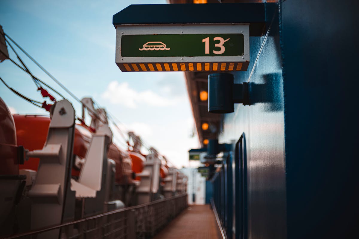 6 Weird Things on Cruise Ships Most Passengers Never Expect to Find 4 Close-up of a ship deck showing a green sign with a lifeboat symbol and the number 13.
