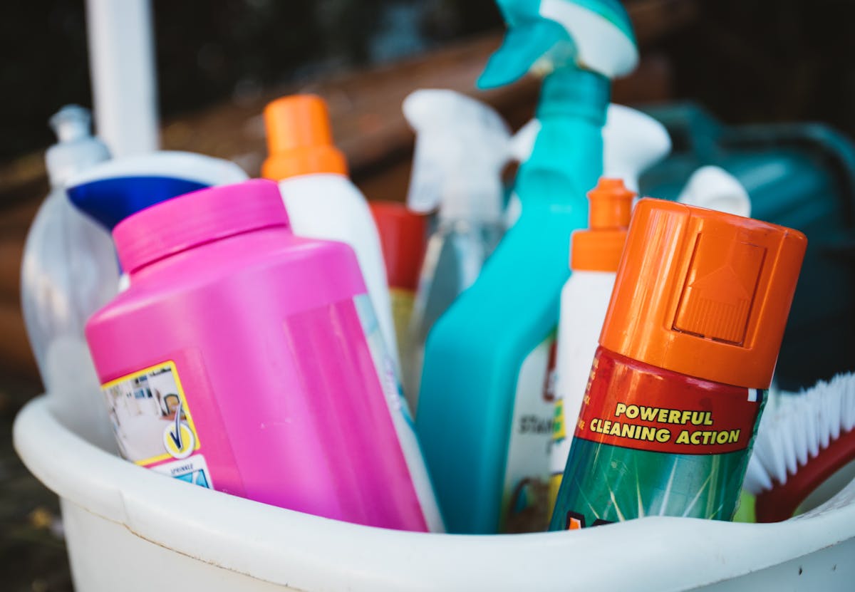 8 Spring Cleaning Mistakes You’re Probably Making 3 Close-up of assorted cleaning supplies in a bucket outdoors, showcasing various detergents and sprays.