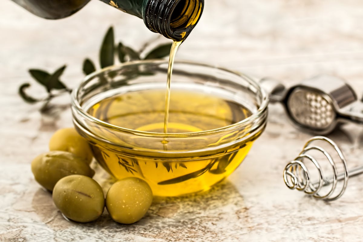 10 School Facts Boomers Learned That Turned Out to Be Wrong 1 Close-up of olive oil being poured into a glass bowl surrounded by fresh olives and kitchen tools.