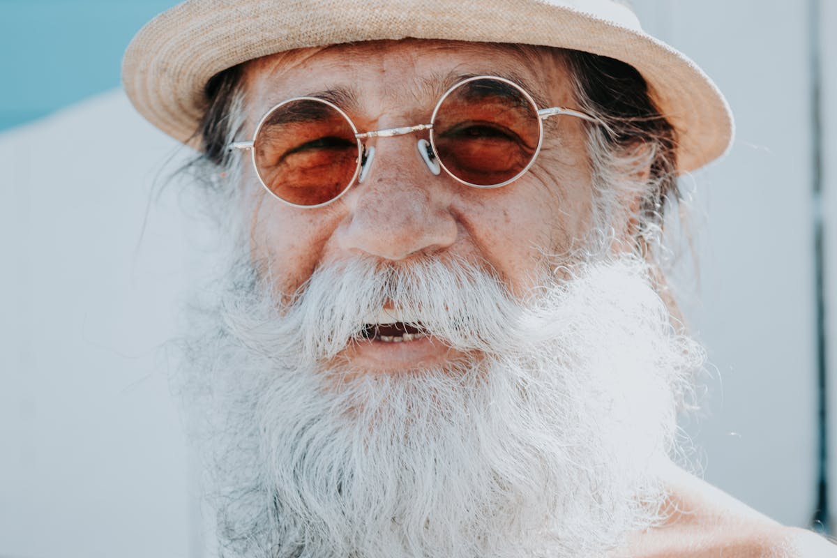 10 Weird Things Governments Actually Taxed 2 Close-up portrait of a smiling senior man with a long beard, wearing a hat and sunglasses.