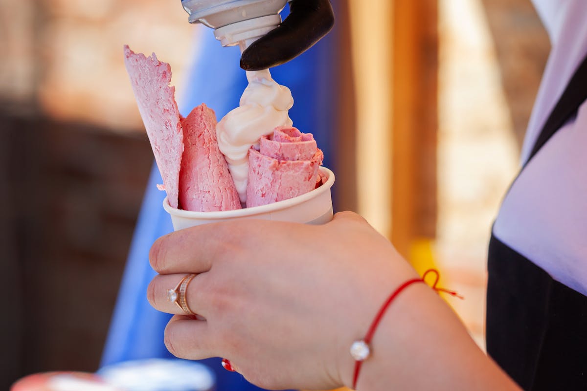 The Wildest Food and Condiment Mishaps That Escalated Into Chaos 1 Delicious rolled ice cream being topped with soft cream, held by a person with jewelry.