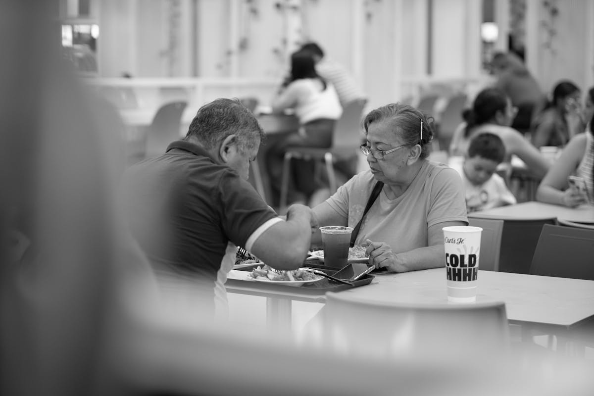 10 Baby Boomer Behaviors That Annoy Millennials and Gen Z 2 Elderly couple enjoying a meal at a fast food restaurant in a bustling food court.
