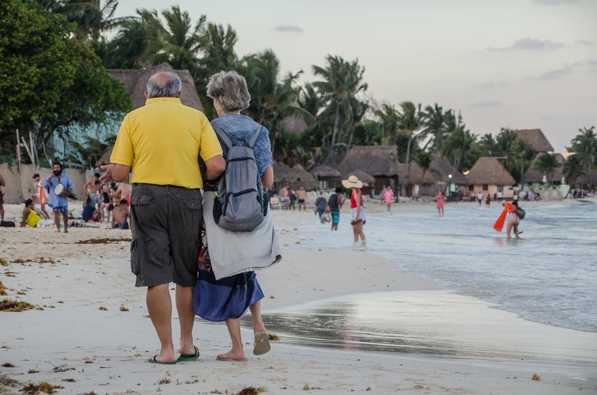 10 Baby Boomer Behaviors That Annoy Millennials and Gen Z 3 Elderly couple enjoying a peaceful walk on a tropical beach at sunset.