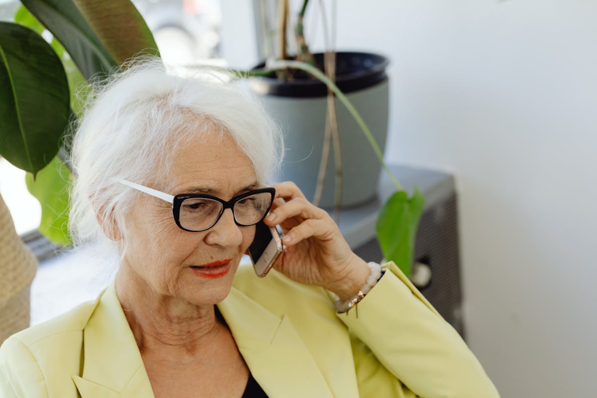 10 Baby Boomer Behaviors That Annoy Millennials and Gen Z 1 Elderly woman with white hair and eyeglasses using cellphone indoors.
