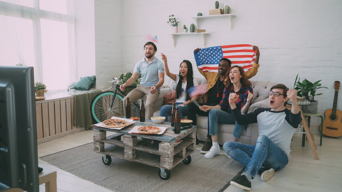 11 Outrageous Trends That Defined the Last Decade 2 Group of diverse friends cheering for a sports event with American flags indoors.