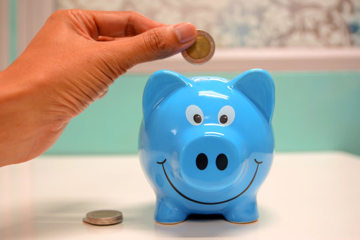 8 Money Myths That Are Actually Keeping You Poor 1 Hand inserting a coin into a blue piggy bank for savings and money management.