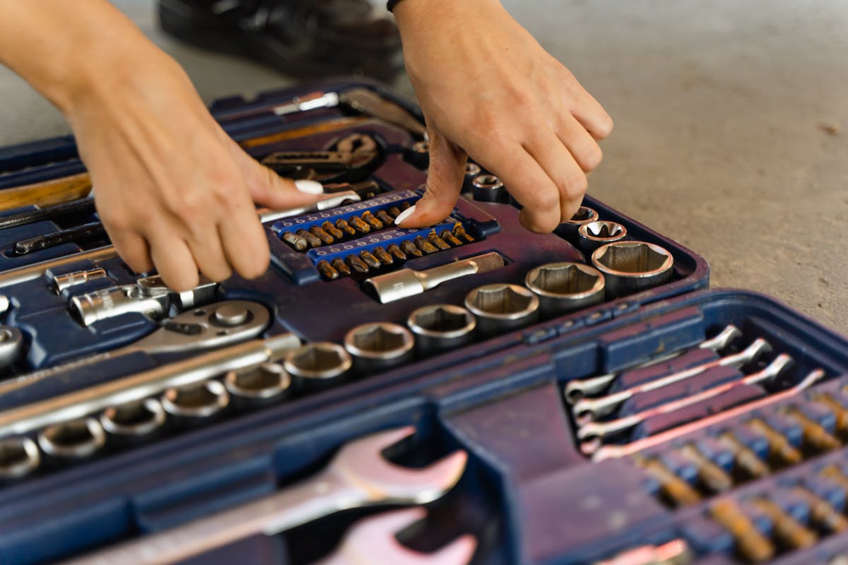 8 Items You Should Stop Storing In Kitchen Cabinets 2 Hands selecting tools from a well-organized toolbox on a concrete surface.