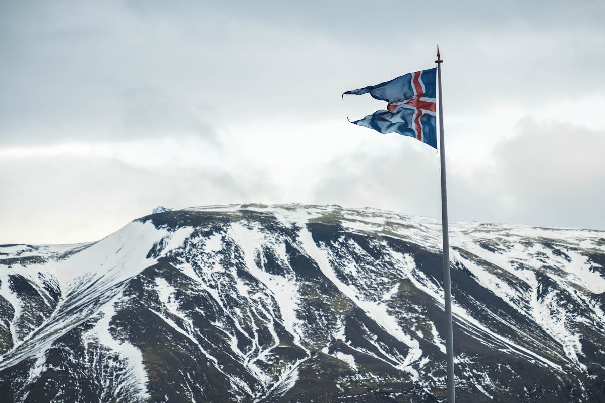 10 Political Scandals That Shook Nations and Triggered Mass Uprisings 1 Icelandic flag flying against a backdrop of snow-covered mountains, capturing Iceland's natural beauty.